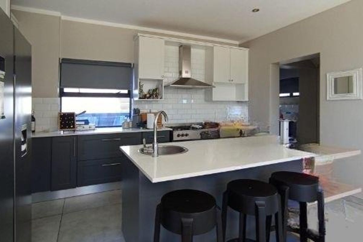 Modern kitchen featuring a central island with a sink, stone countertops, subway tile backsplash, and stainless steel extractor fan.