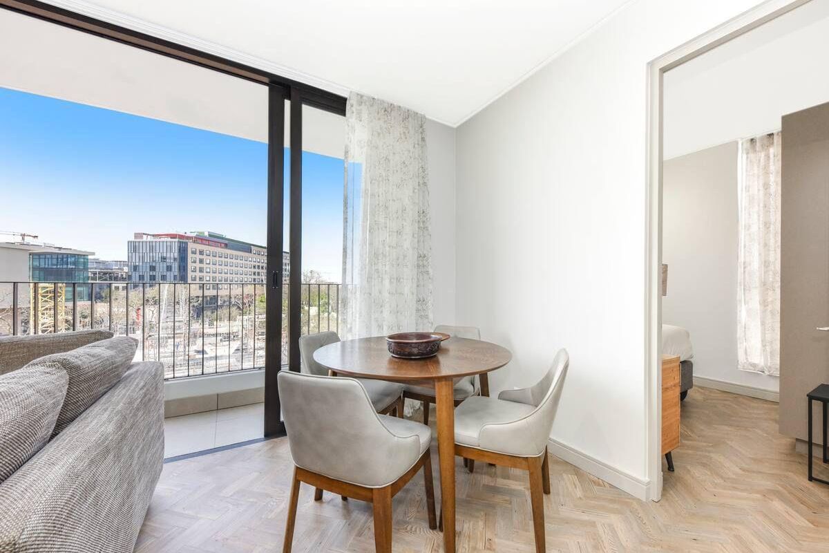 Bright living area featuring elegant herringbone timber flooring and large sliding glass doors opening onto a private balcony with urban views.