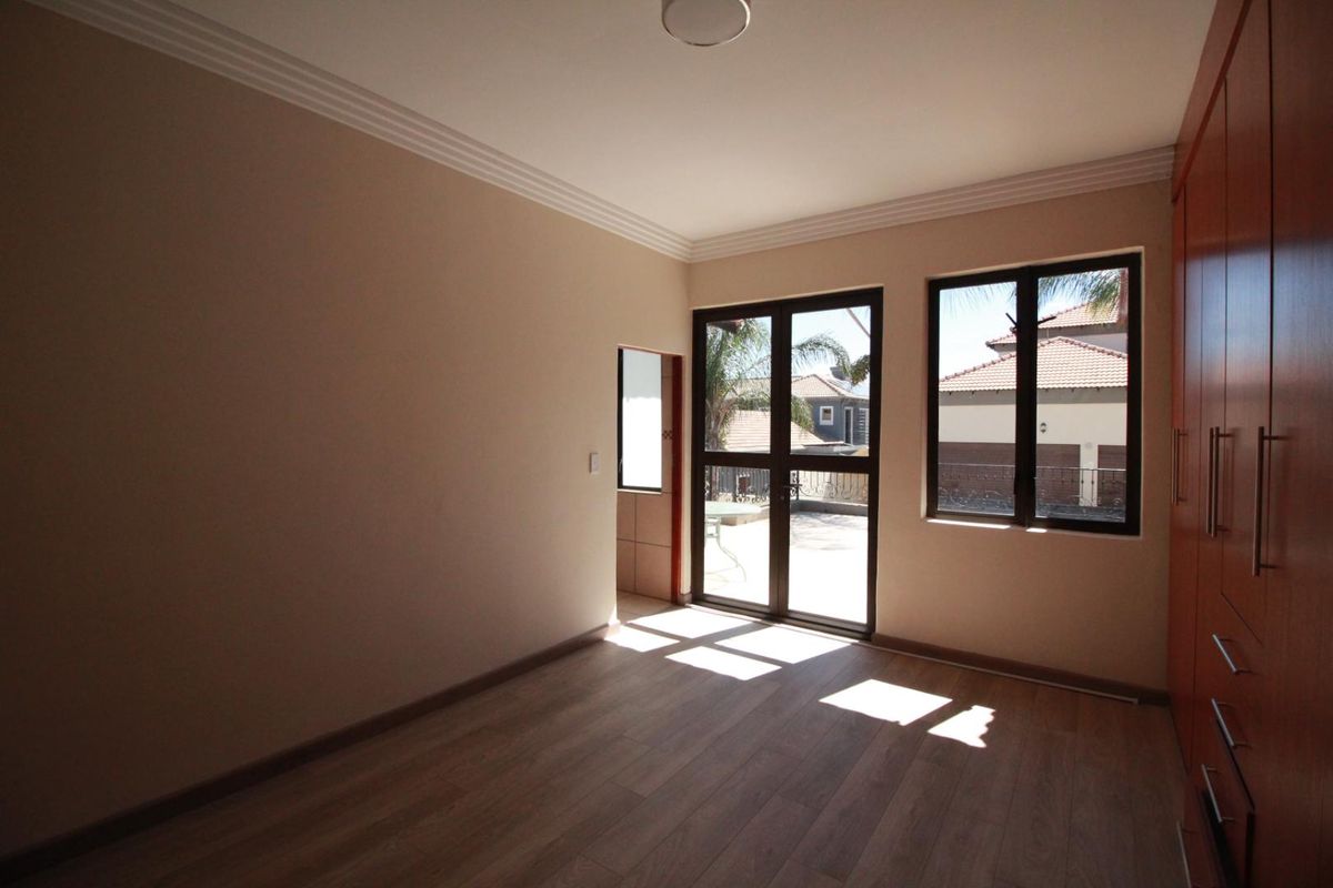A bright, empty bedroom featuring modern laminate flooring, built-in cupboards, and direct access to an outdoor patio area through glass doors.