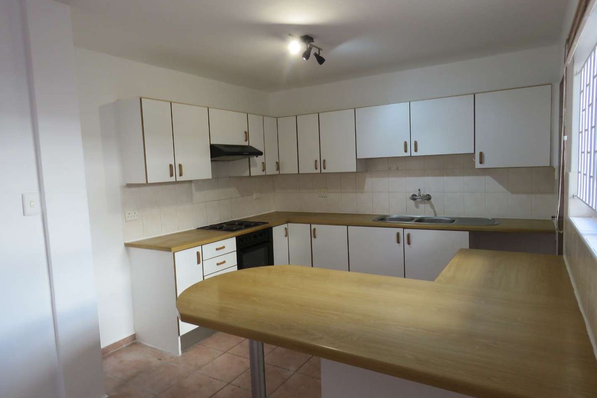 A functional kitchen featuring white cabinetry, wood-look laminate countertops, a breakfast bar, and integrated appliances including an oven, hob, and extractor fan.