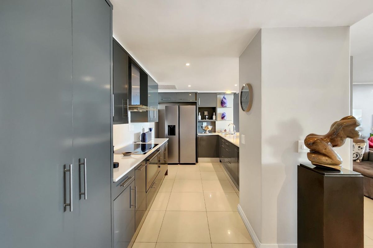 Modern galley-style kitchen featuring sleek grey cabinetry, stone countertops, integrated appliances, and polished tile flooring, offering a clean and contemporary aesthetic.