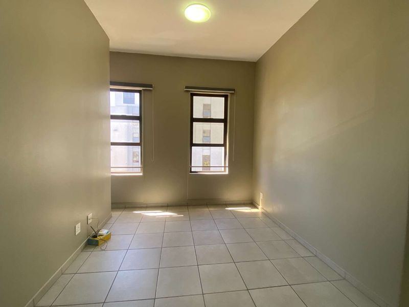 A bright, empty bedroom featuring neutral wall paint, tiled flooring, and two windows with roller blinds, offering a clean canvas for personalization.