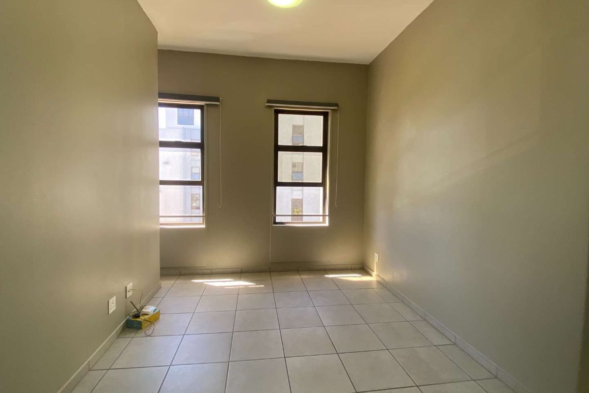 A bright, empty bedroom featuring neutral wall paint, tiled flooring, and two windows with roller blinds, offering a clean canvas for personalization.