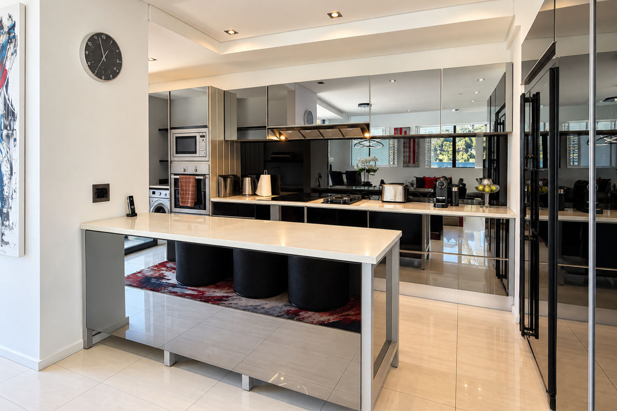 Modern kitchen featuring a stone island, integrated appliances, mirrored splashback, and sleek cabinetry, offering a sophisticated and functional culinary space.