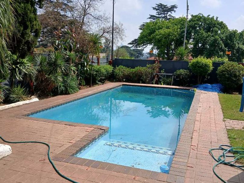 Outdoor swimming pool area featuring brick paving surround and established garden perimeter.