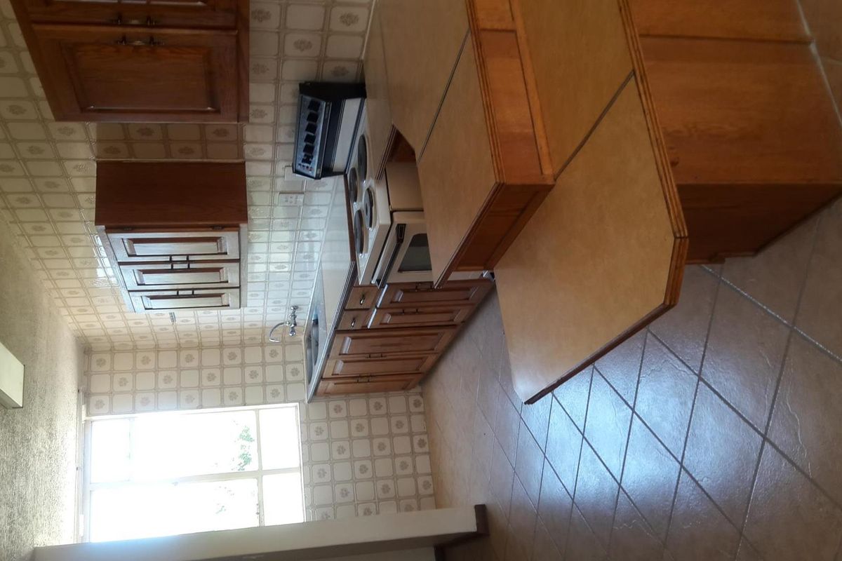 A functional kitchen featuring wooden cabinetry, tiled backsplash, and tiled flooring, equipped with a built-in oven, hob, and extractor fan.