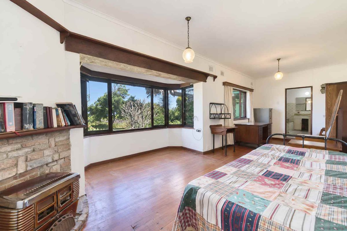 Spacious bedroom featuring a large bay window, timber flooring, and a classic brick fireplace, offering a bright and character-filled living space.