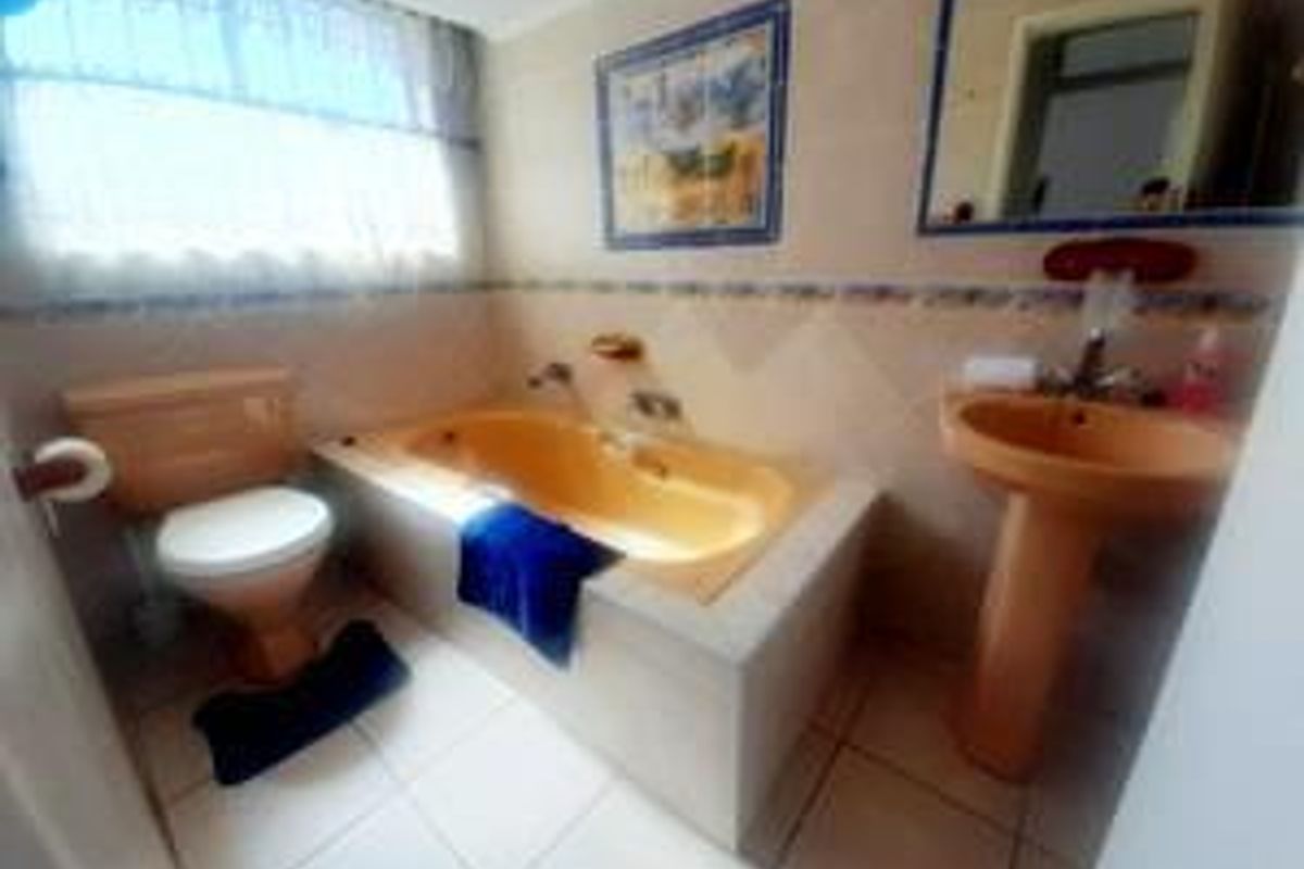 A dated bathroom featuring a built-in bathtub, pedestal basin, and toilet with tiled finishes throughout.