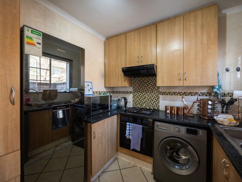 Compact kitchen featuring laminate cabinetry, granite countertops, mosaic tile backsplash, built-in oven, hob, extractor fan, and tiled flooring.