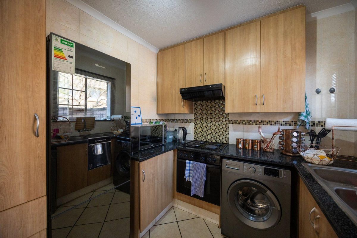 Compact kitchen featuring laminate cabinetry, granite countertops, mosaic tile backsplash, built-in oven, hob, extractor fan, and tiled flooring.