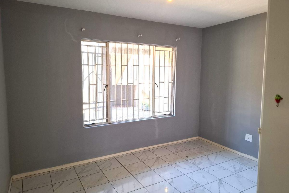 An empty bedroom featuring grey painted walls, white marble-look floor tiles, and a large window fitted with security burglar bars.