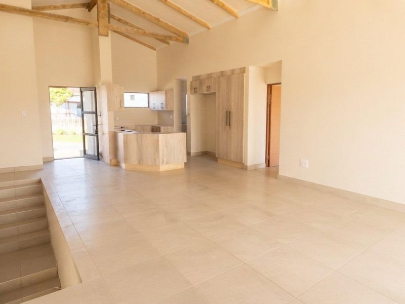 Spacious open-plan living area featuring vaulted ceilings with exposed timber beams, tiled flooring, and a modern kitchen with built-in cabinetry.
