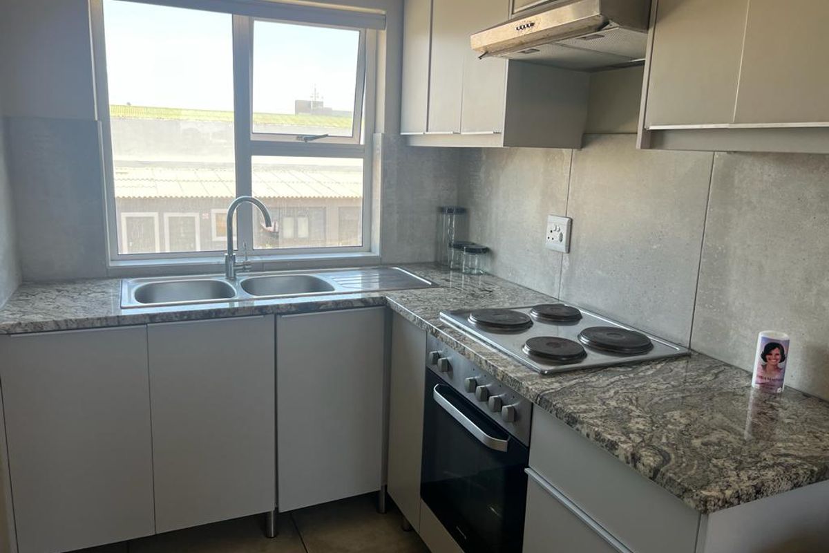 Compact kitchen featuring granite countertops, stainless steel double sink, built-in electric oven, hob, and overhead extractor fan with neutral cabinetry.