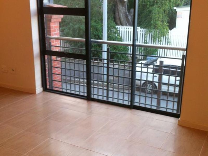 An empty living room featuring neutral tiled flooring and a large sliding glass door leading to a balcony with metal railings.