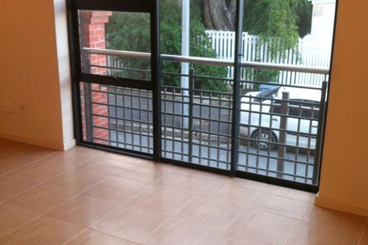 An empty living room featuring neutral tiled flooring and a large sliding glass door leading to a balcony with metal railings.