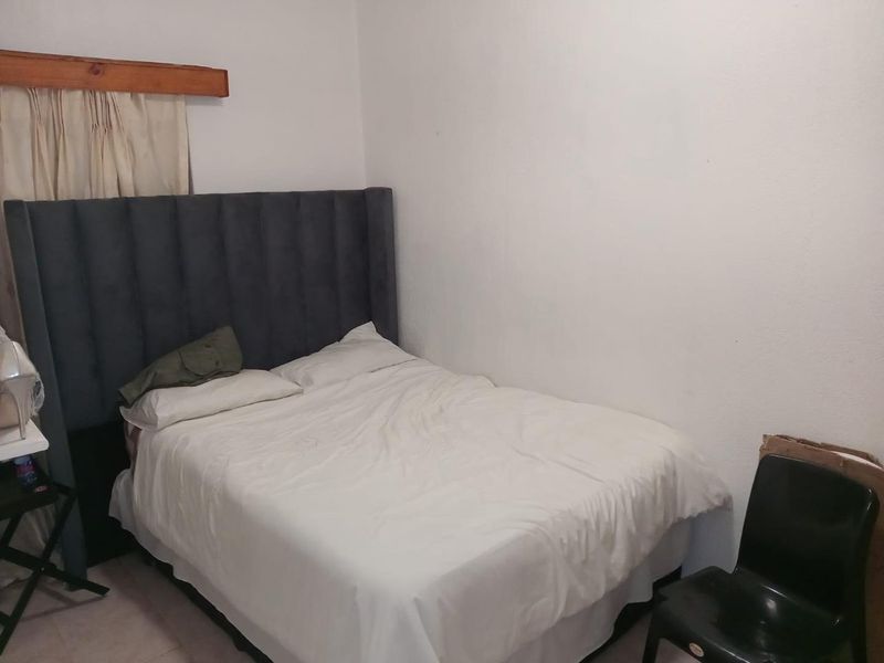 A simple bedroom featuring plain white walls and a wooden curtain pelmet above the window area.