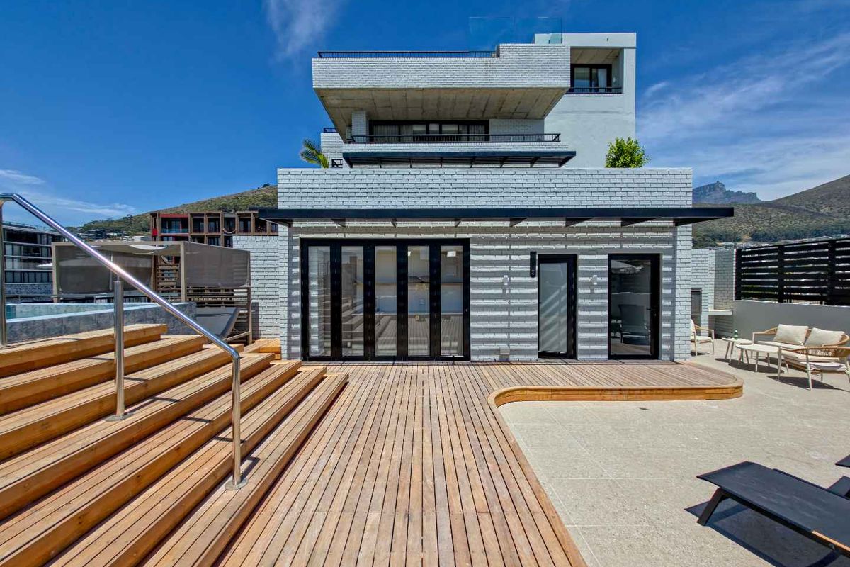 A modern multi-level apartment exterior featuring timber decking, a swimming pool, and bi-fold doors leading into the living space.