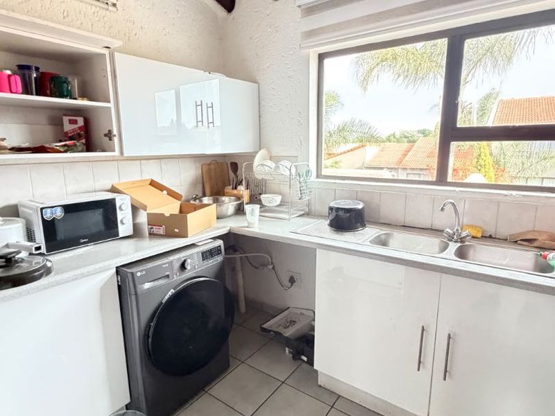 A functional kitchen featuring exposed timber ceiling beams, tiled flooring, laminate countertops, and a double bowl stainless steel sink with a view.