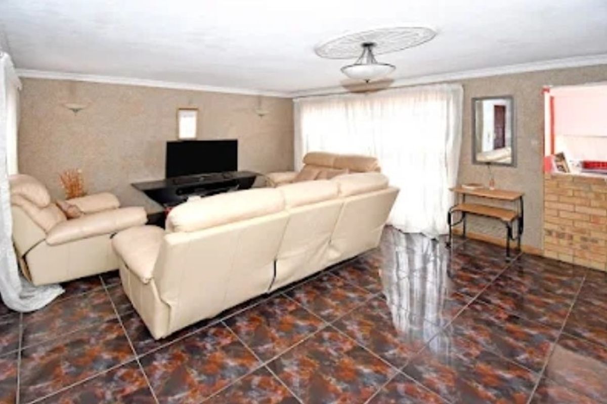 Spacious living room featuring dark patterned ceramic floor tiles, a decorative ceiling rose, and a brick feature wall with access to an outdoor area.