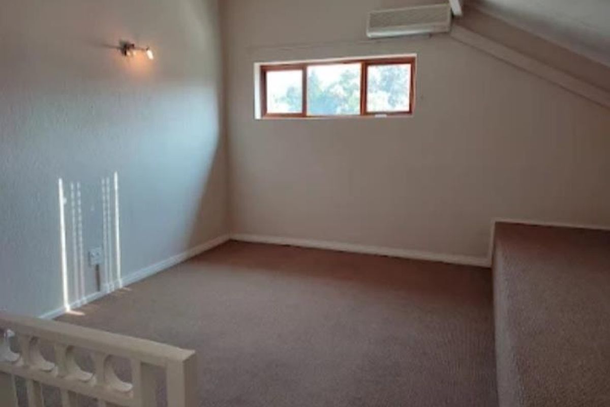 An attic-style bedroom featuring carpeted flooring, a split-system air conditioning unit, and a raked ceiling with a small window.