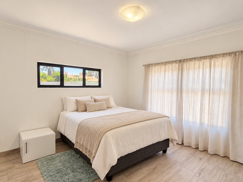 A bright and well-maintained bedroom featuring neutral walls, crown molding, tiled flooring, and large windows with integrated curtain tracks.