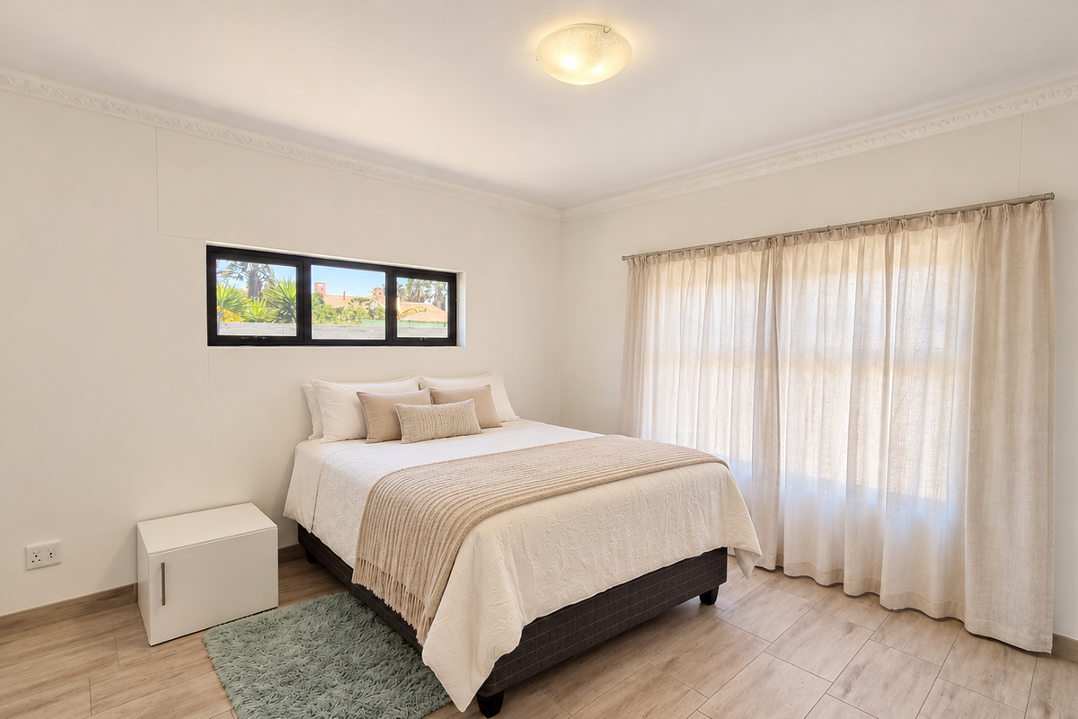A bright and well-maintained bedroom featuring neutral walls, crown molding, tiled flooring, and large windows with integrated curtain tracks.