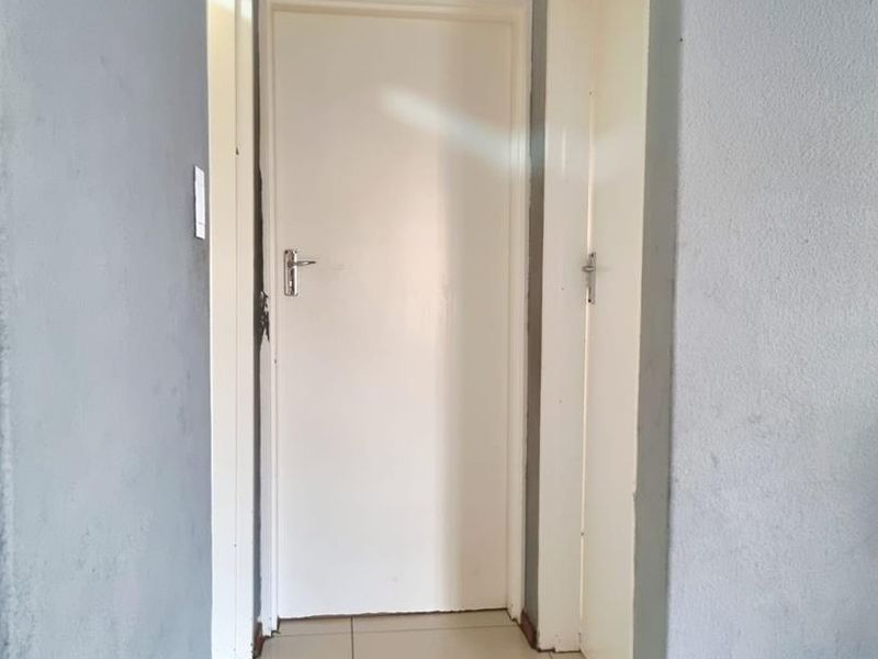 A functional hallway featuring tiled flooring, neutral grey walls, and access to multiple rooms via standard interior doors.