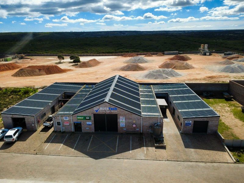 Aerial view of a commercial automotive workshop facility featuring a brick exterior, extensive solar panel installation, and a paved parking area.
