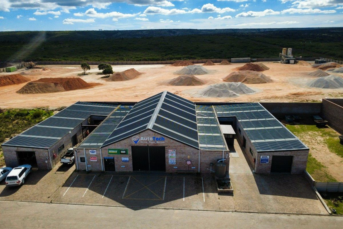 Aerial view of a commercial automotive workshop facility featuring a brick exterior, extensive solar panel installation, and a paved parking area.