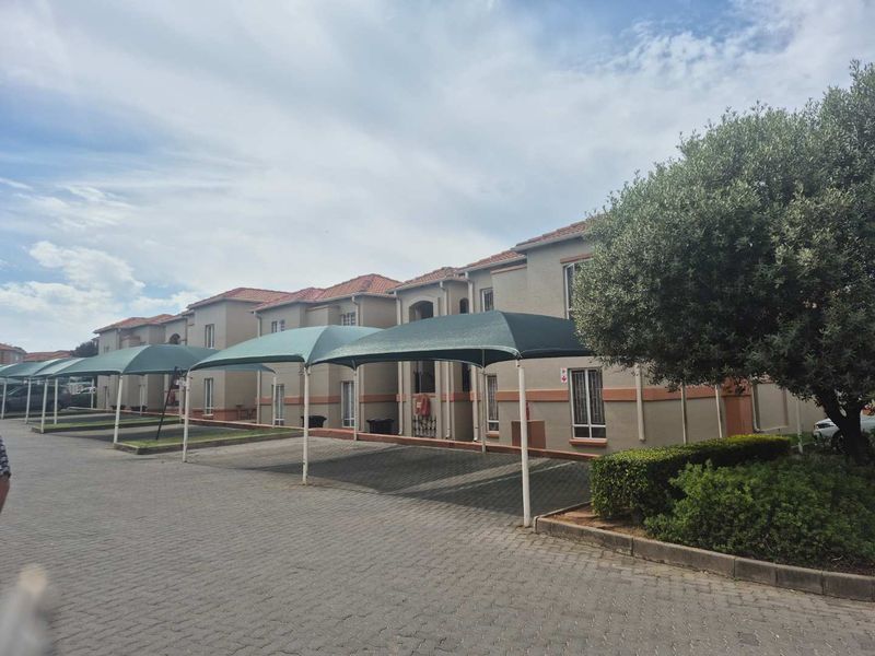 Exterior view of a townhouse complex featuring paved driveway access and dedicated shade cloth carport parking bays.
