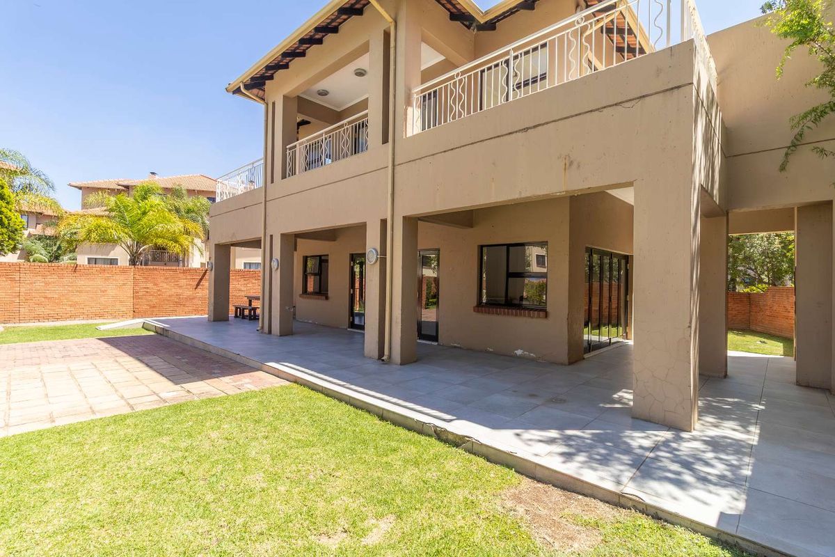 Spacious rear exterior view featuring a covered patio, tiled flooring, and a balcony overlooking the private garden area.