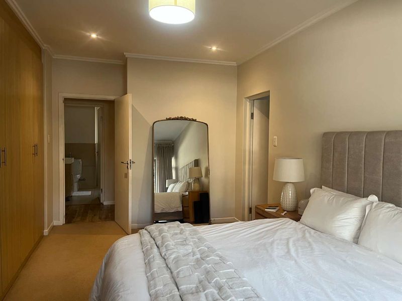 A well-maintained bedroom featuring built-in cupboards, neutral carpeting, and recessed lighting, with an adjoining en-suite bathroom visible through the doorway.