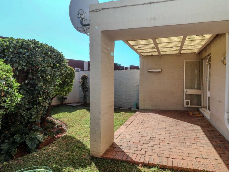 A covered brick-paved patio area overlooking a small private garden, featuring a structural pillar and integrated pet door access.