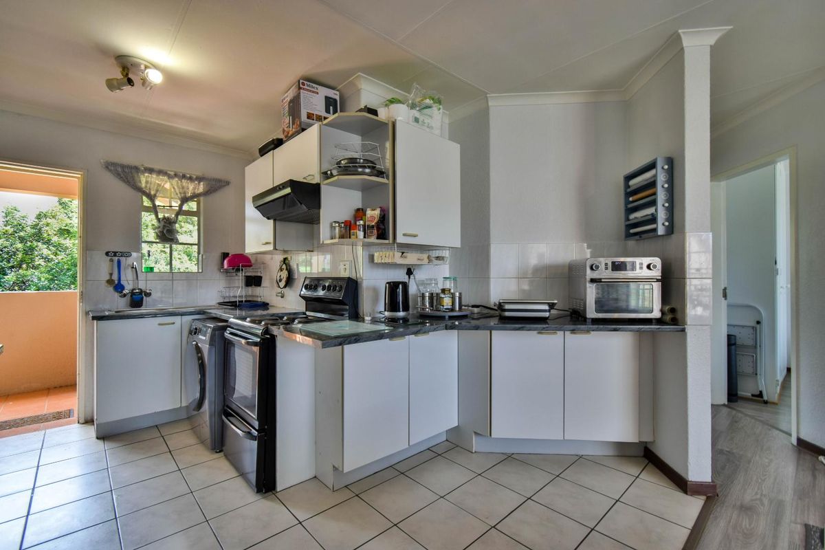 Functional kitchen featuring white cabinetry, tiled countertops, integrated stove and extractor fan, with direct access to an outdoor patio area.