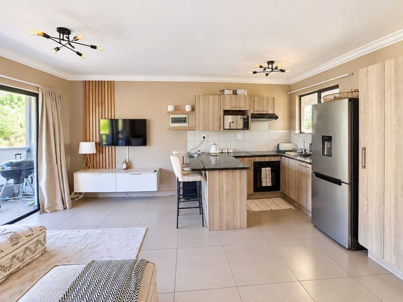 Modern open-plan living area featuring a contemporary kitchen with granite countertops, built-in appliances, and seamless access to an outdoor balcony.