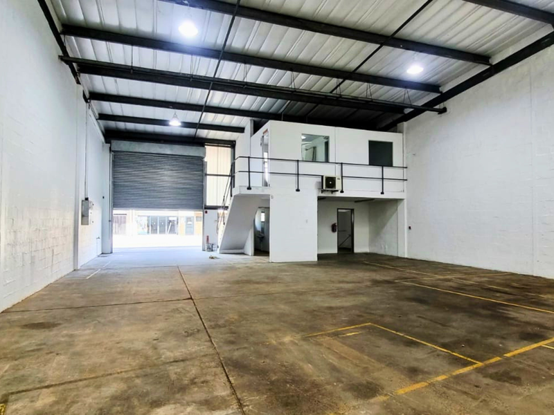 Spacious industrial warehouse unit featuring a high-clearance ceiling, roller shutter door access, and a functional mezzanine office level with stairs.