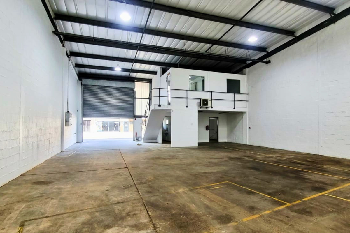 Spacious industrial warehouse unit featuring a high-clearance ceiling, roller shutter door access, and a functional mezzanine office level with stairs.