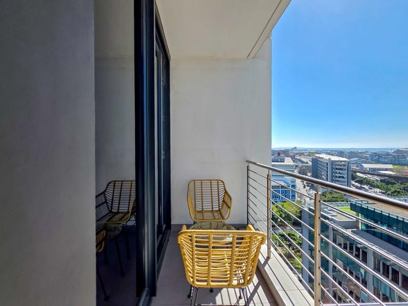 A modern apartment balcony featuring a stainless steel balustrade and expansive city and ocean views.