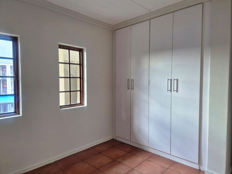 A clean, empty bedroom featuring built-in cupboards, tiled flooring, and wooden window frames, offering a neutral space ready for personalization.