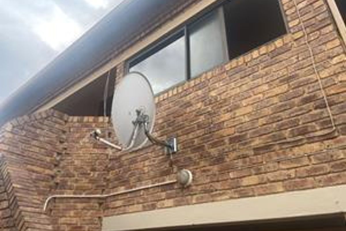 Exterior view of the face brick facade featuring a sliding window, mounted satellite dish, and external lighting fixture.