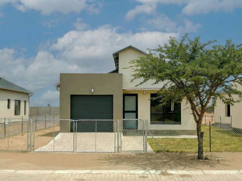Front view of a modern single-story house featuring a paved driveway, single garage, and secure perimeter fencing.