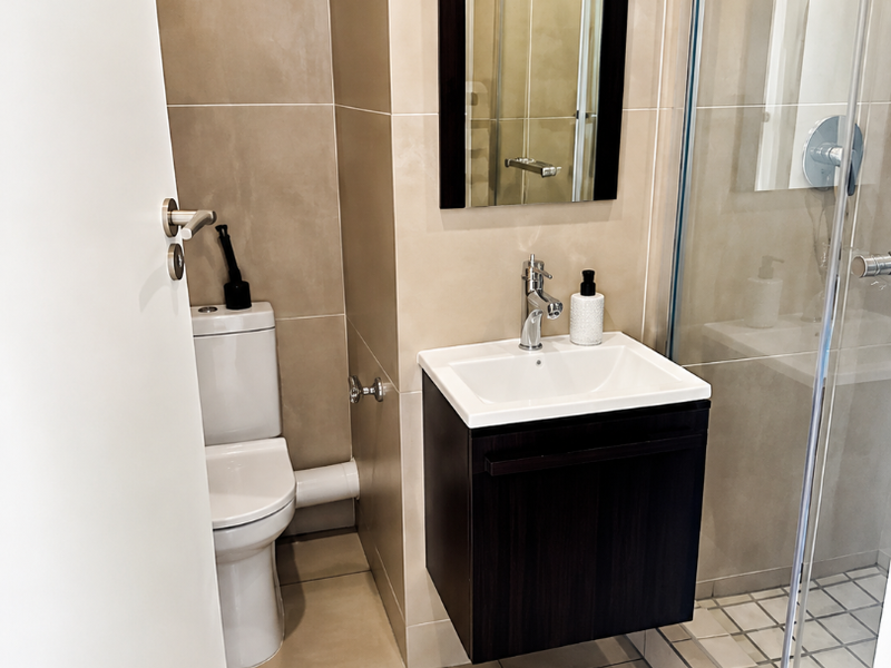 Modern bathroom featuring a wall-mounted vanity, glass shower enclosure, and neutral ceramic tiling throughout.
