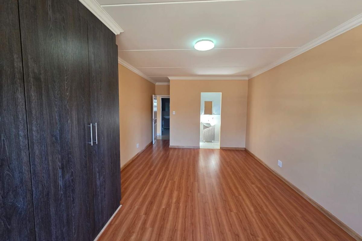 A spacious, empty bedroom featuring wood-look laminate flooring, built-in dark wood cabinetry, and neutral wall tones, with an adjacent doorway leading to a bathroom.
