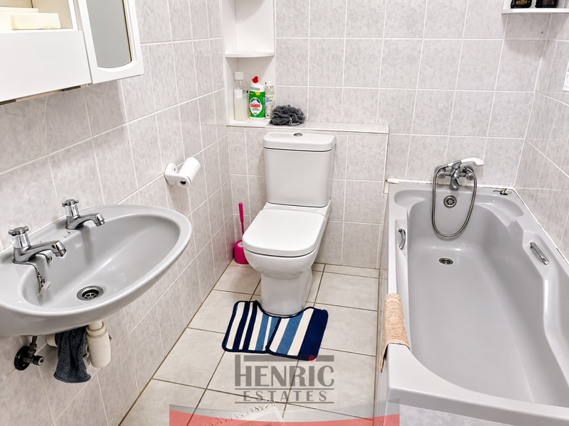 A functional bathroom featuring a pedestal basin, a built-in bathtub with shower mixer, and a wall-mounted toilet, finished with neutral ceramic wall and floor tiles.