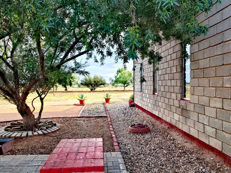 A view of the rear exterior of the farm property, featuring a concrete block wall, gravel landscaping, and a paved walkway under mature trees.