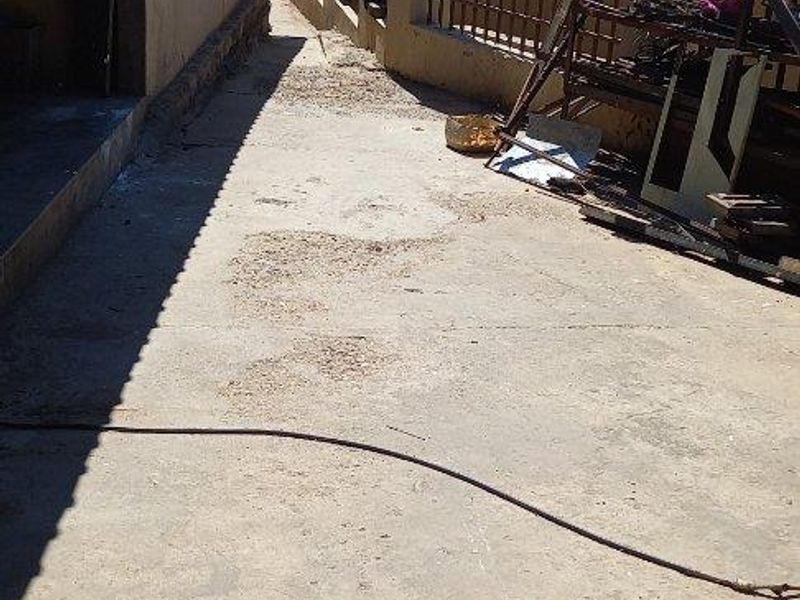 A narrow exterior side or rear passage featuring concrete paving, enclosed by a perimeter fence with masonry pillars and security razor wire.