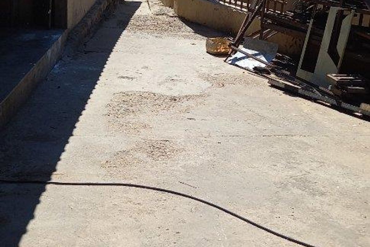 A narrow exterior side or rear passage featuring concrete paving, enclosed by a perimeter fence with masonry pillars and security razor wire.