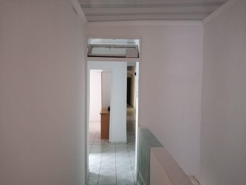 A simple, empty hallway featuring tiled flooring and a corrugated ceiling, providing access to adjacent rooms within the property.