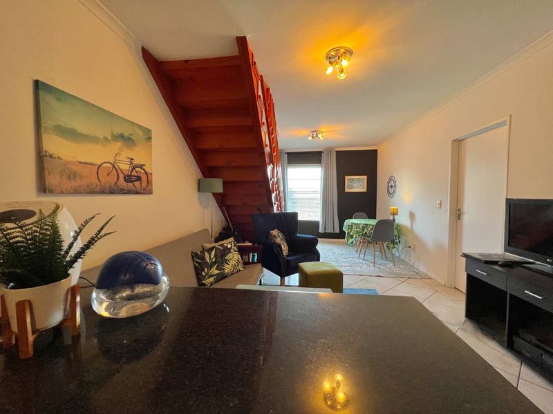 Open plan living and dining area featuring a wooden staircase, tiled flooring, and a granite kitchen counter.