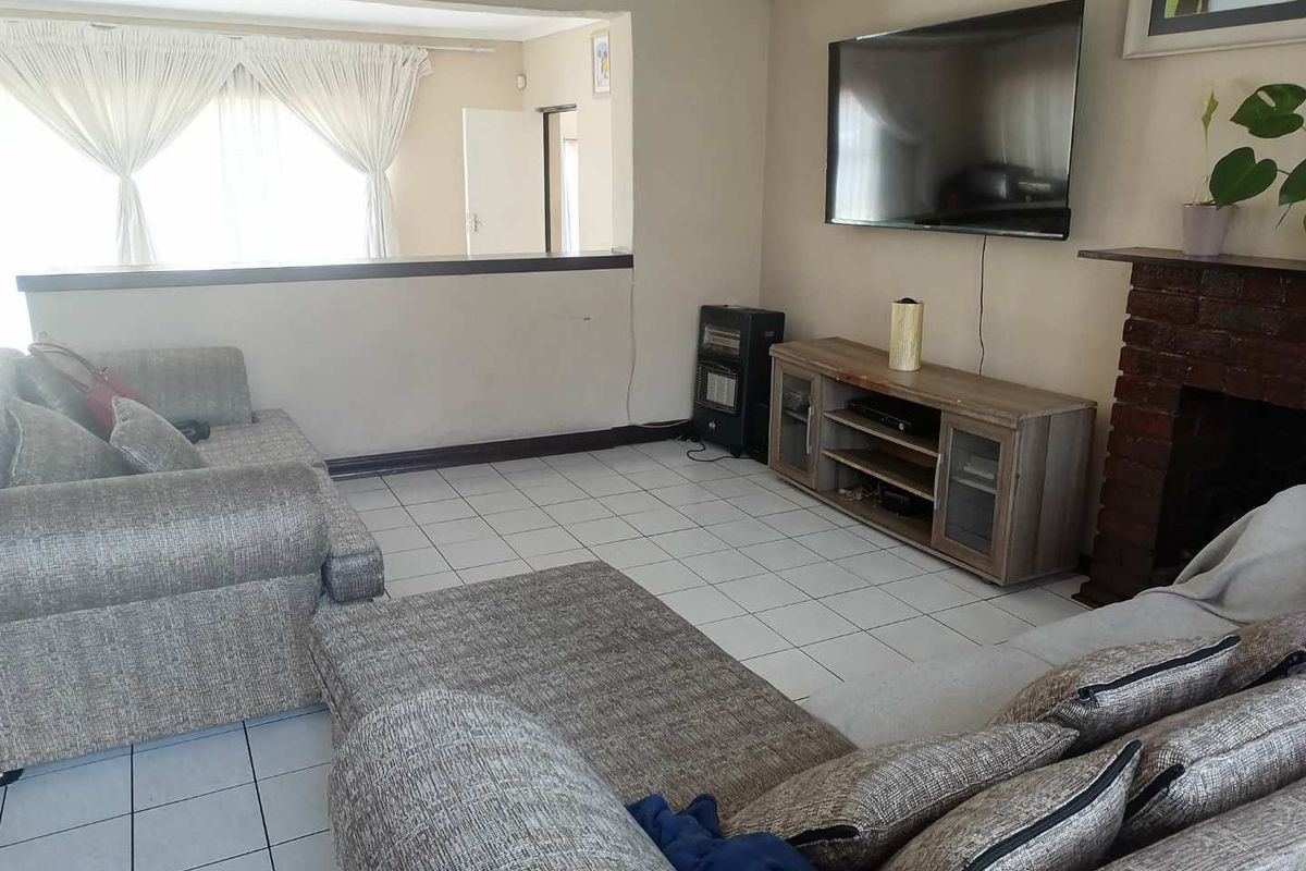 A living room featuring tiled flooring, a brick fireplace, and a half-wall partition separating the space from an adjacent area.